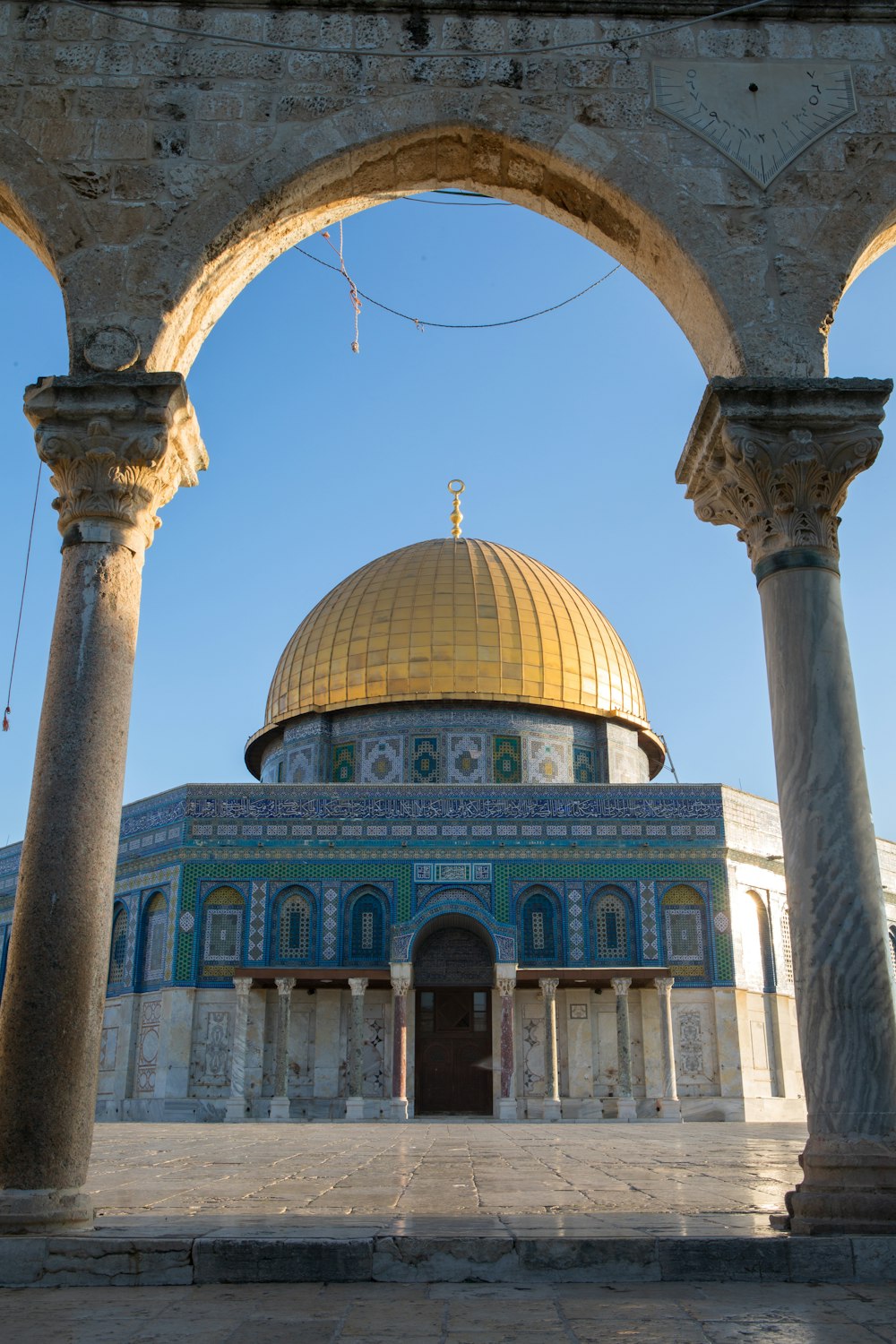 a domed building with columns with Dome of the Rock in the background