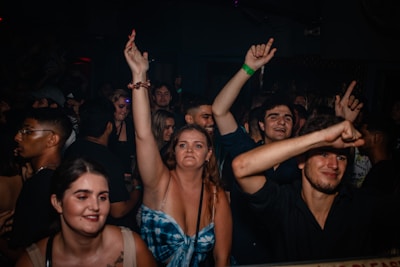 A crowded club scene with people dancing and enjoying themselves. Several individuals are raising their arms in the air, capturing a lively and energetic atmosphere.