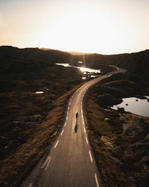 A lone cyclist navigating a dusty mountain trail under a vast, fiery sunset sky.