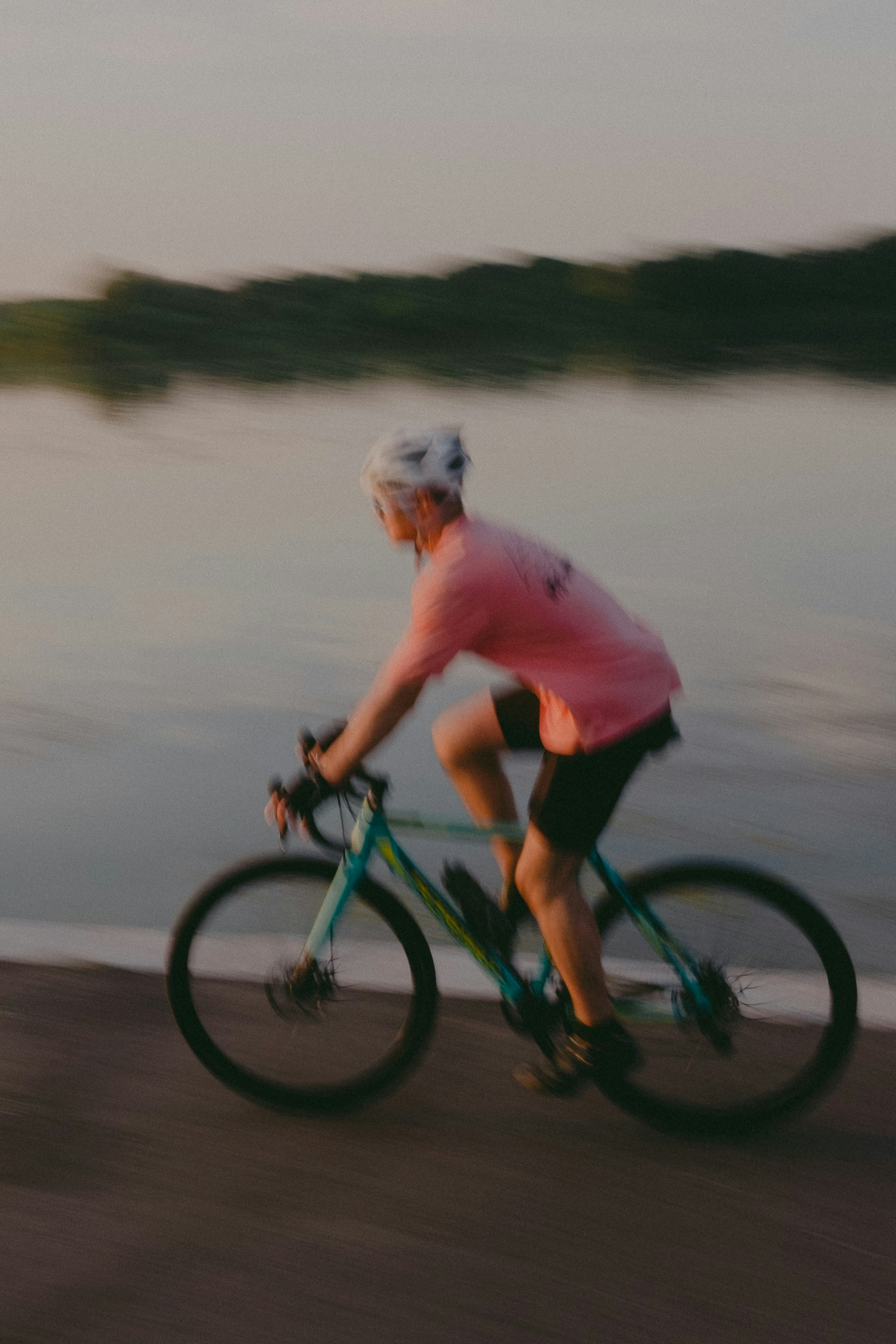Un hombre montando una bicicleta en una carretera junto a un cuerpo de agua