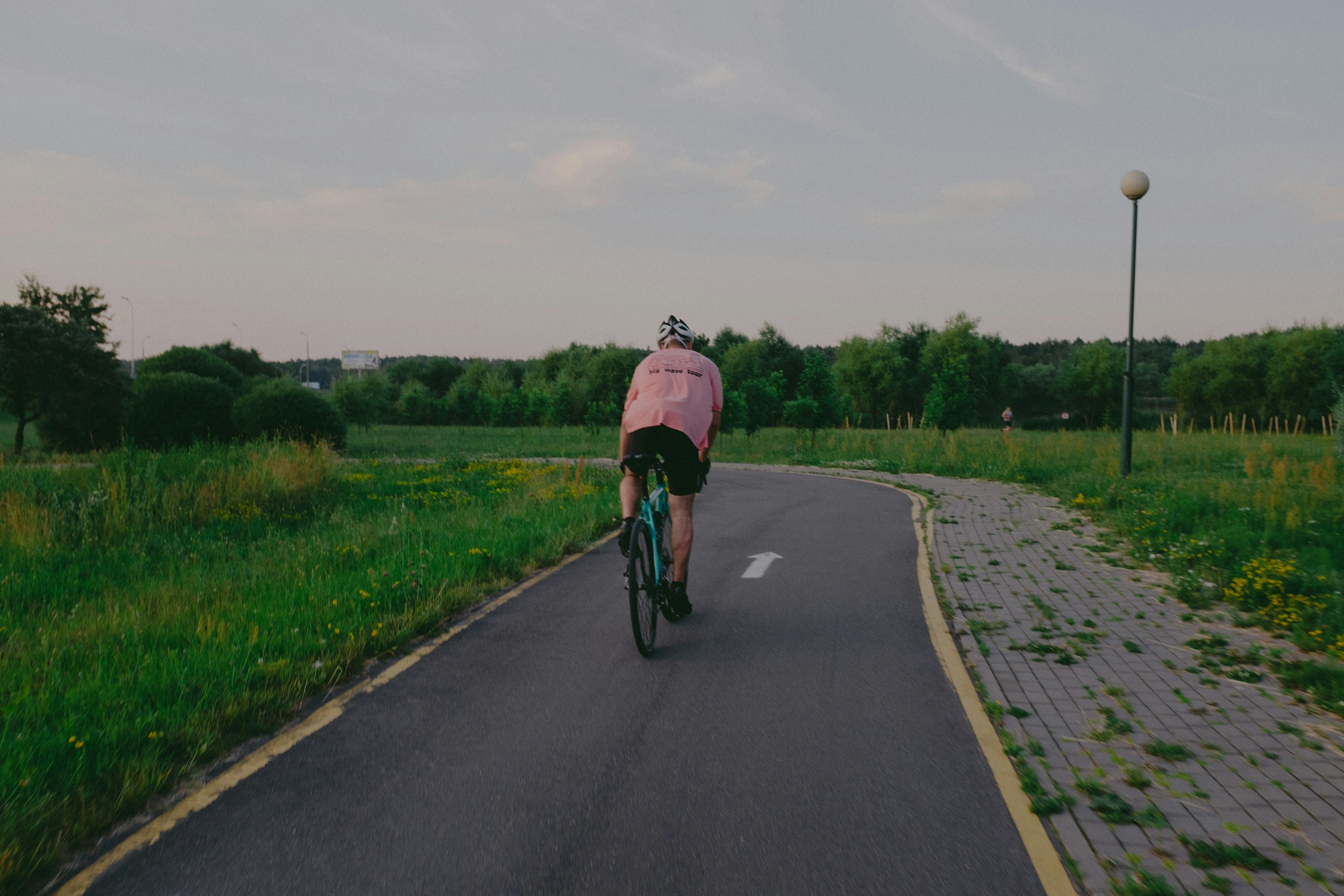 a person riding a bicycle on a road with grass and trees on either side