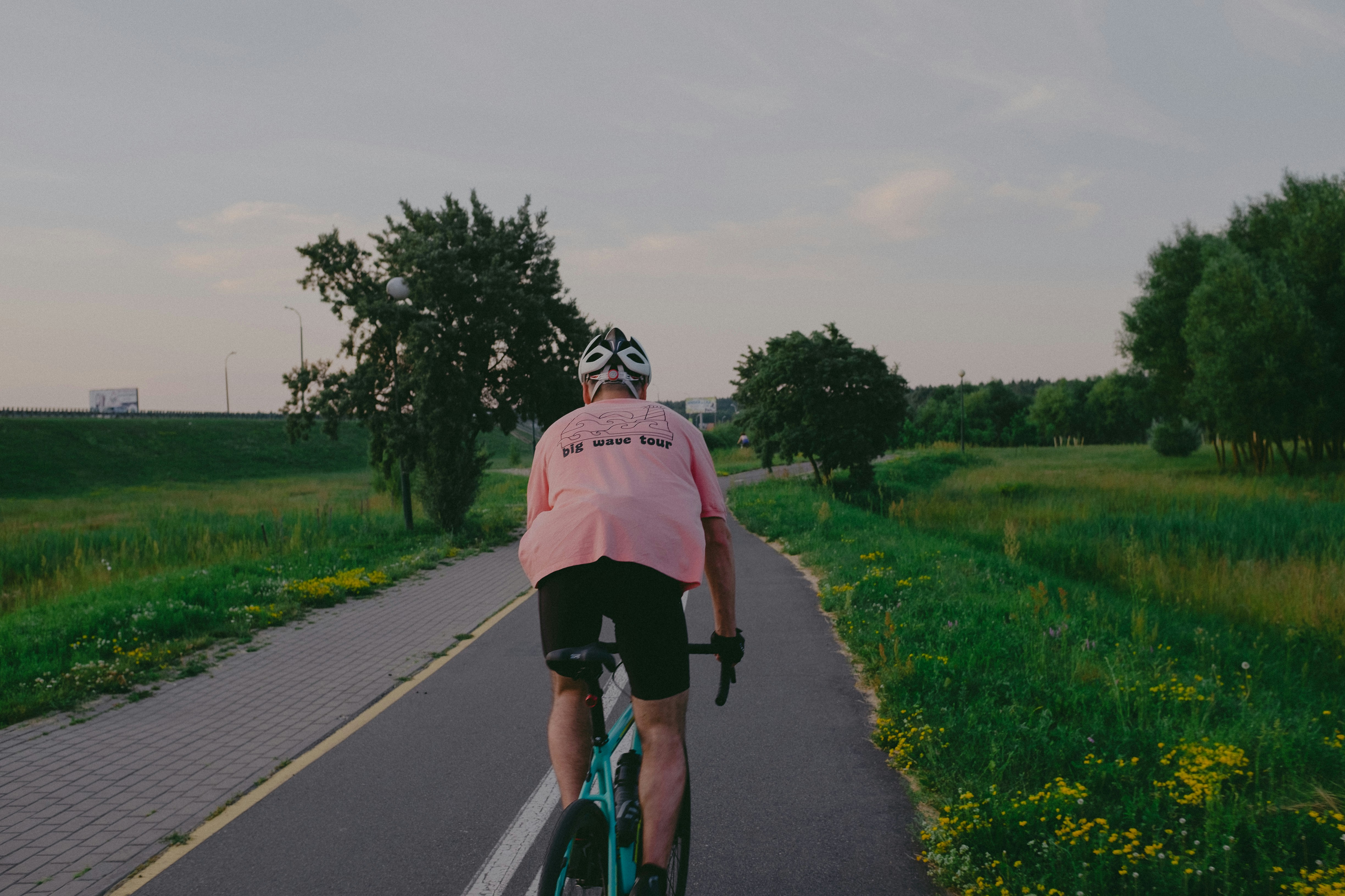 a person riding a bicycle on a road with grass and trees on either side