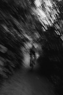 Black and white photo of a cyclist racing down a winding road surrounded by trees.