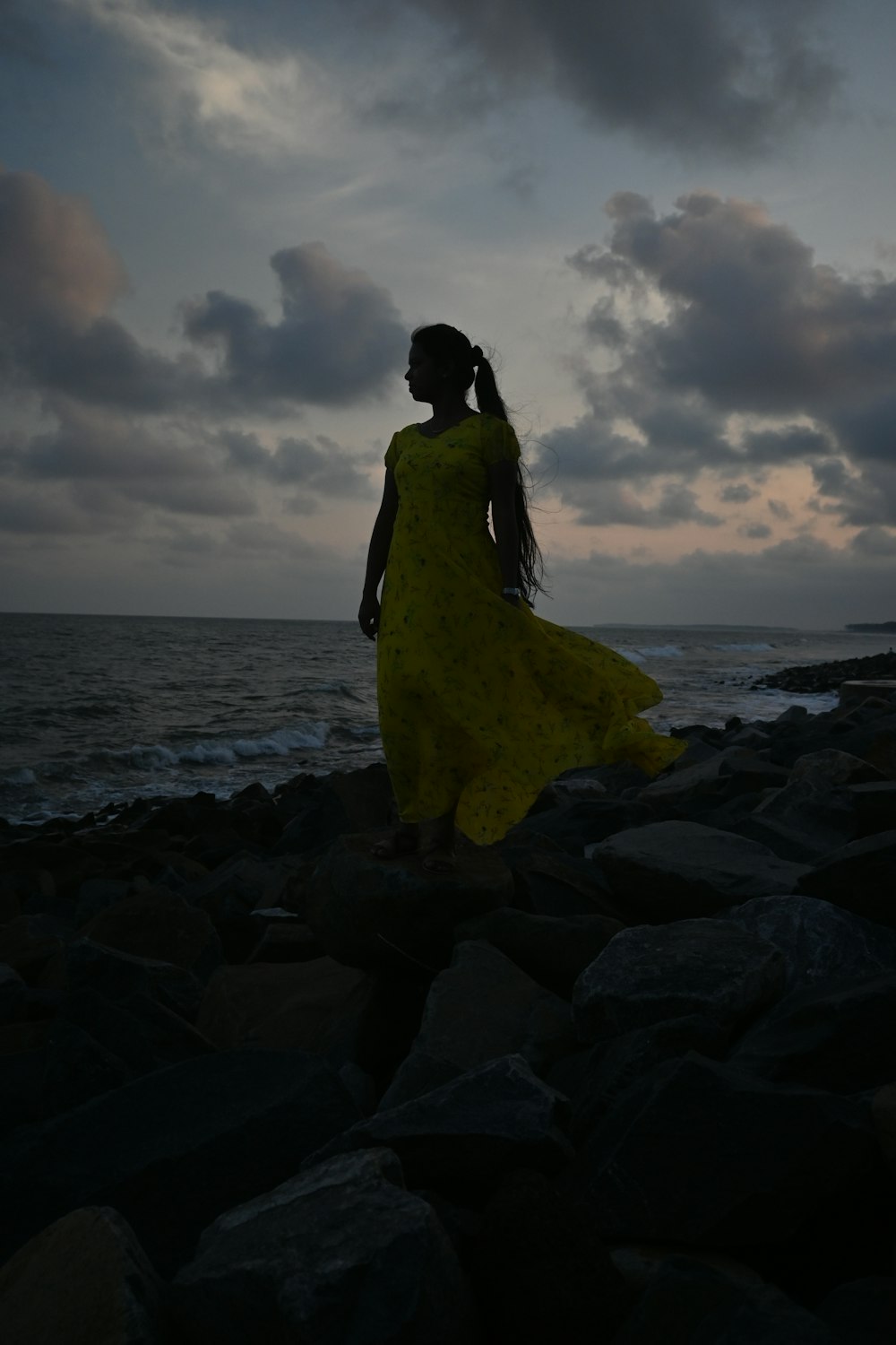 a person in a yellow dress on a rocky beach
