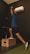 A person is performing a dynamic exercise. They are standing on one leg on a wooden box while holding a kettlebell overhead. The background is a dark gym with an air conditioning unit on the wall.
