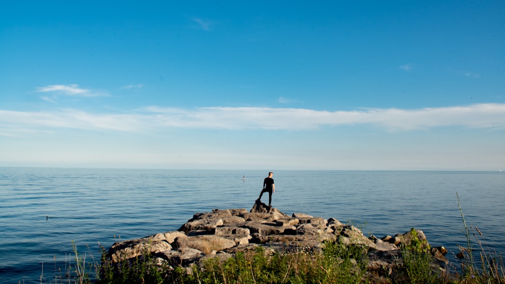 uma pessoa de pé em uma rocha ao lado da água