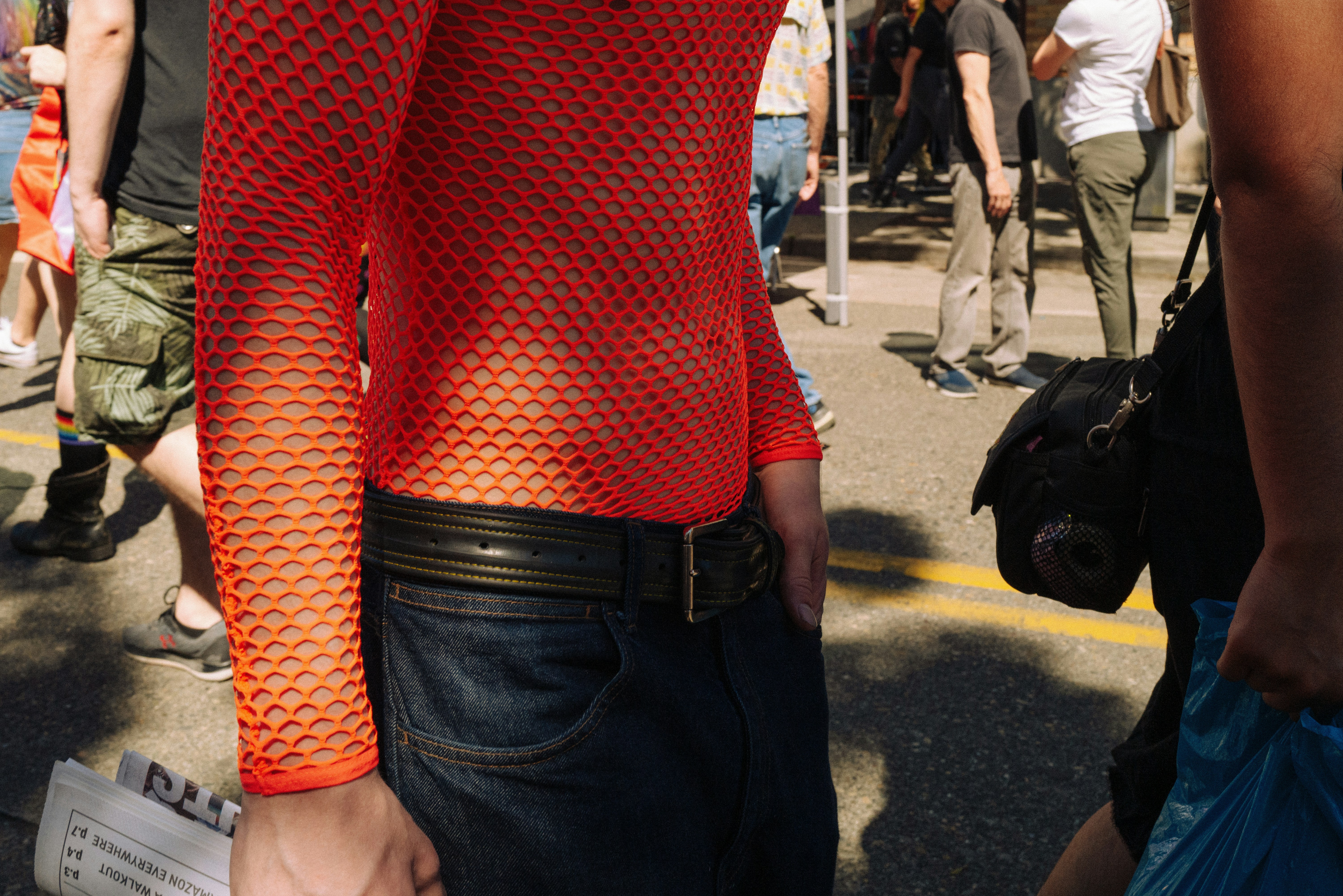 Person wearing a red mesh top holds a newspaper outdoors.
