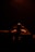 A person is silhouetted against a dark background, illuminated by a warm, soft light. The individual appears to be adjusting headphones, suggesting a focus on sound or music. The environment is dimly lit, creating a dramatic and intimate atmosphere.
