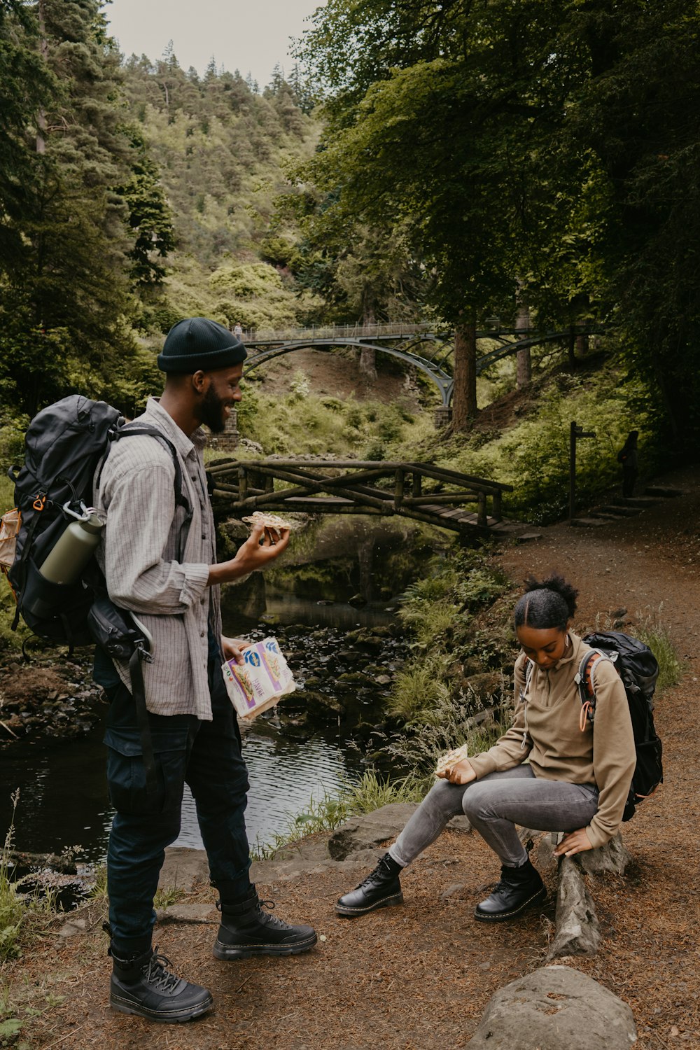 a man sitting next to a man eating food by a river