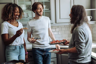 Group of friends enjoying a pizza night at home, wearing chef hats and laughing around the table.