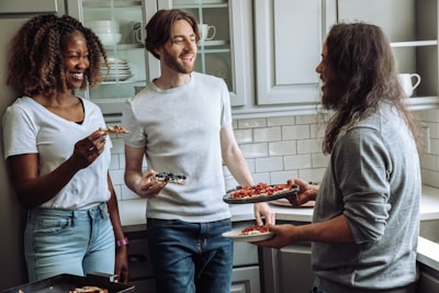 Friends laughing and sharing slices of pizza around a cozy table lit by warm ambient lighting.