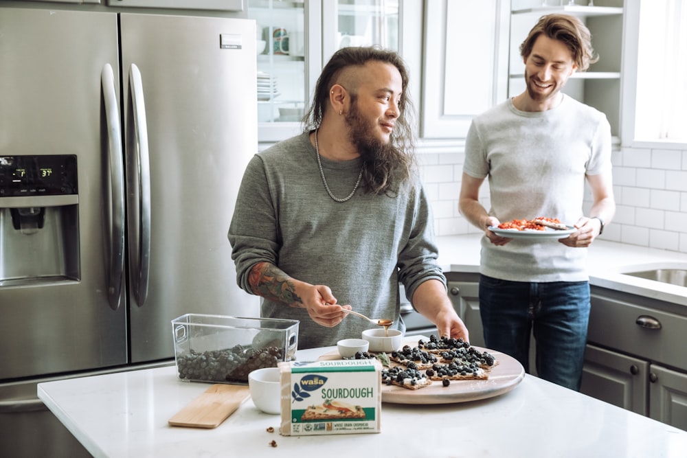 a couple of men stand near each other holding pizzas