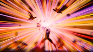 A dynamic and vibrant burst of colors radiates from the center, creating a sense of motion and energy. Silhouettes of people are scattered, seemingly propelled outward by the central explosion of light and color.