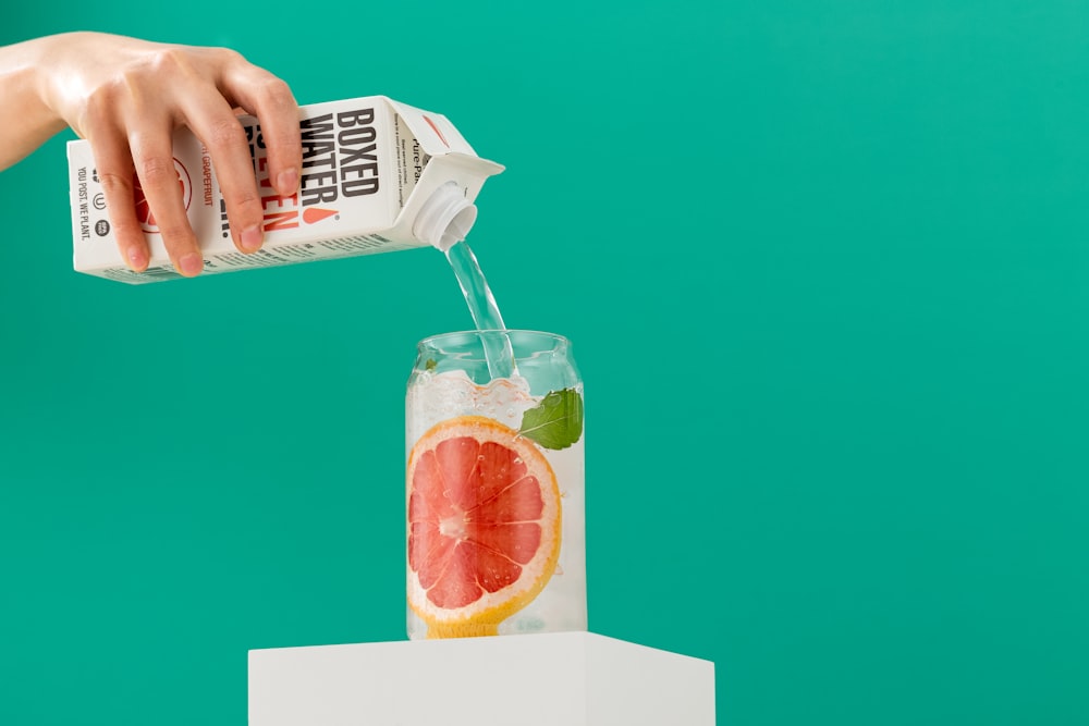 a hand holding a plastic bag over a glass of orange juice