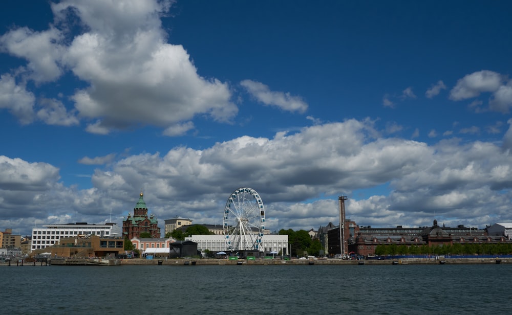 a body of water with buildings and a ferris wheel in the background