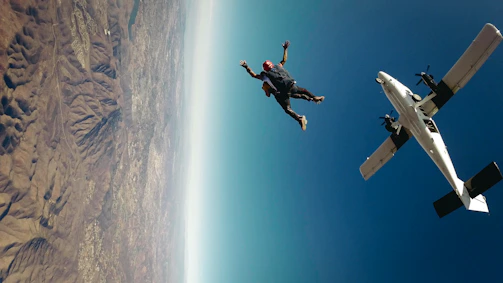 A skydiver free-falling over a vast landscape with mountains and rivers below.