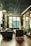 A cozy, well-decorated room featuring modern furniture, including a sofa, chairs, and a round table. The room has a patterned ceiling and large windows allowing natural light. The atmosphere is elegant with decorative items on shelves and a soft color palette.