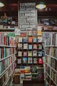 A well-organized bookstore shelf filled with a variety of books. The central section has a display with books displayed with covers facing forward, showcasing titles from different genres and authors. Above the books, there is a large sign featuring the names of famous authors in bold, such as William Shakespeare and Jane Austen. The surrounding shelves are filled with more books arranged side-by-side.
