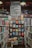 A well-organized bookstore shelf filled with a variety of books. The central section has a display with books displayed with covers facing forward, showcasing titles from different genres and authors. Above the books, there is a large sign featuring the names of famous authors in bold, such as William Shakespeare and Jane Austen. The surrounding shelves are filled with more books arranged side-by-side.