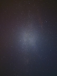 A vast expanse of the night sky filled with countless stars, with a subtle concentration of milky, nebulous light at the center suggesting the presence of a galaxy.