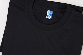 A neatly folded black T-shirt with a blue and white label displaying the size XL. The shirt is made of cotton and is set against a plain background.