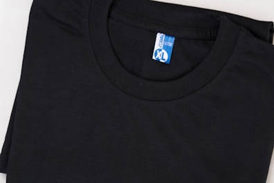 A neatly folded black T-shirt with a blue and white label displaying the size XL. The shirt is made of cotton and is set against a plain background.