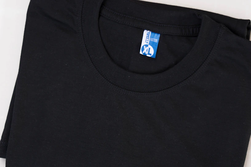 A neatly folded black T-shirt with a blue and white label displaying the size XL. The shirt is made of cotton and is set against a plain background.