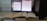 A workspace featuring a computer monitor displaying two digital documents. Next to it, several open books are stacked, and the computer tower is positioned nearby. The monitor shows one document in a PDF reader and another in a word processor.
