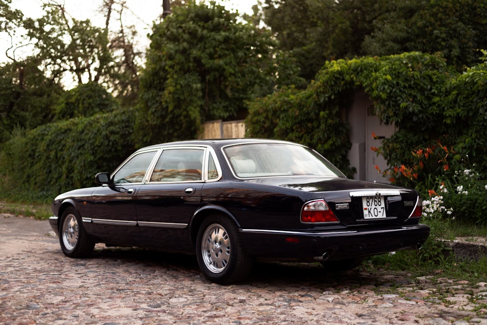 a black car parked in front of a bush and trees