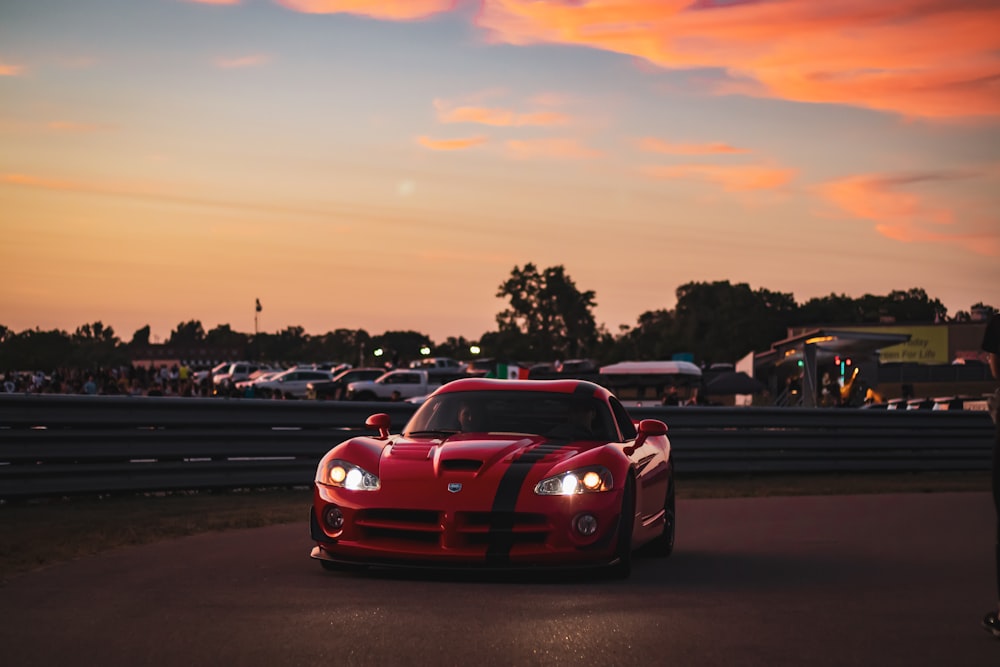 a red sports car parked on a road with other cars and trees in the background