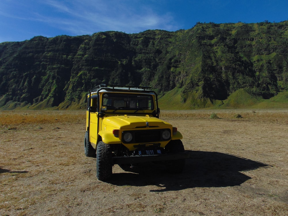 a yellow truck parked on a dirt road with trees and mountains in the background