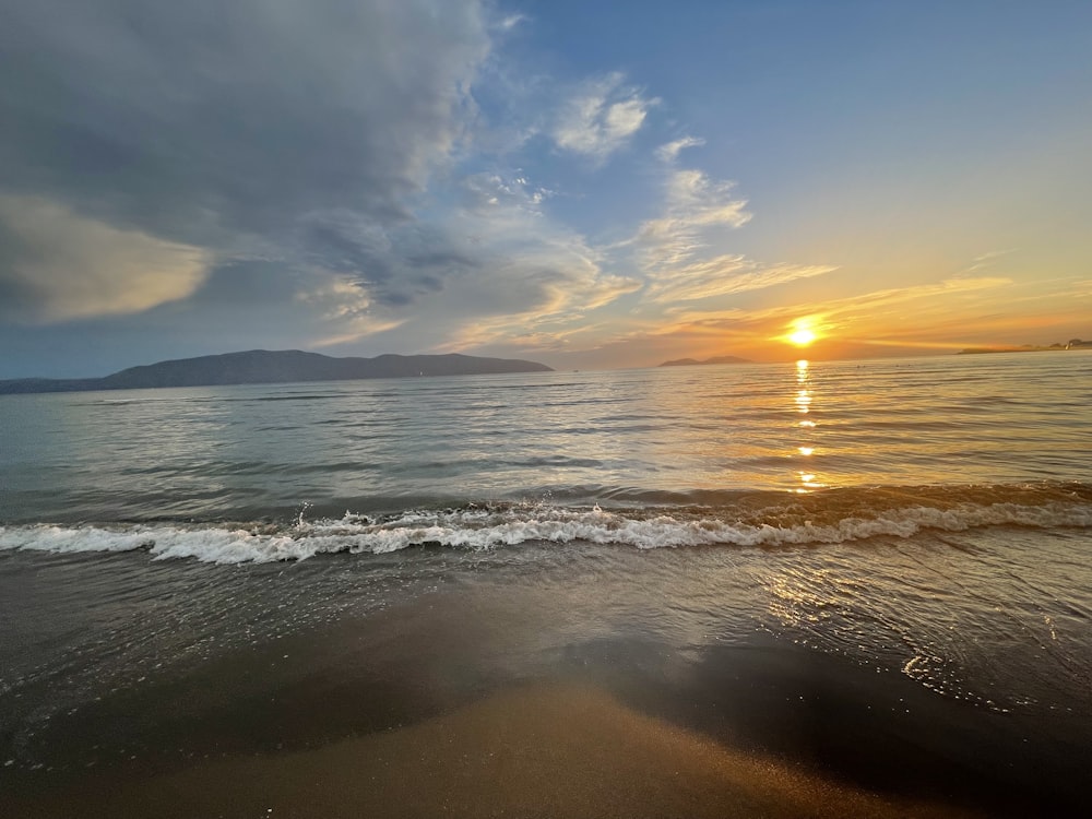 a beach with waves and the sun setting