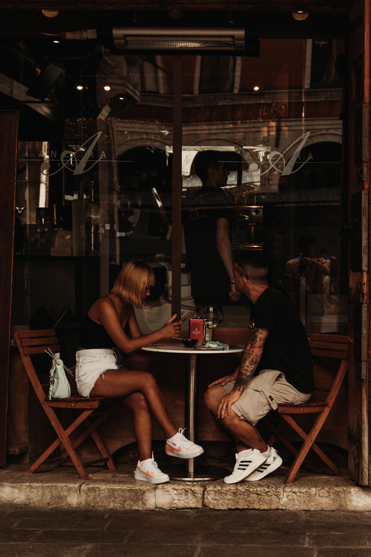 Couple sitting together at an outdoor cafe table chatting and checking a phone on a date