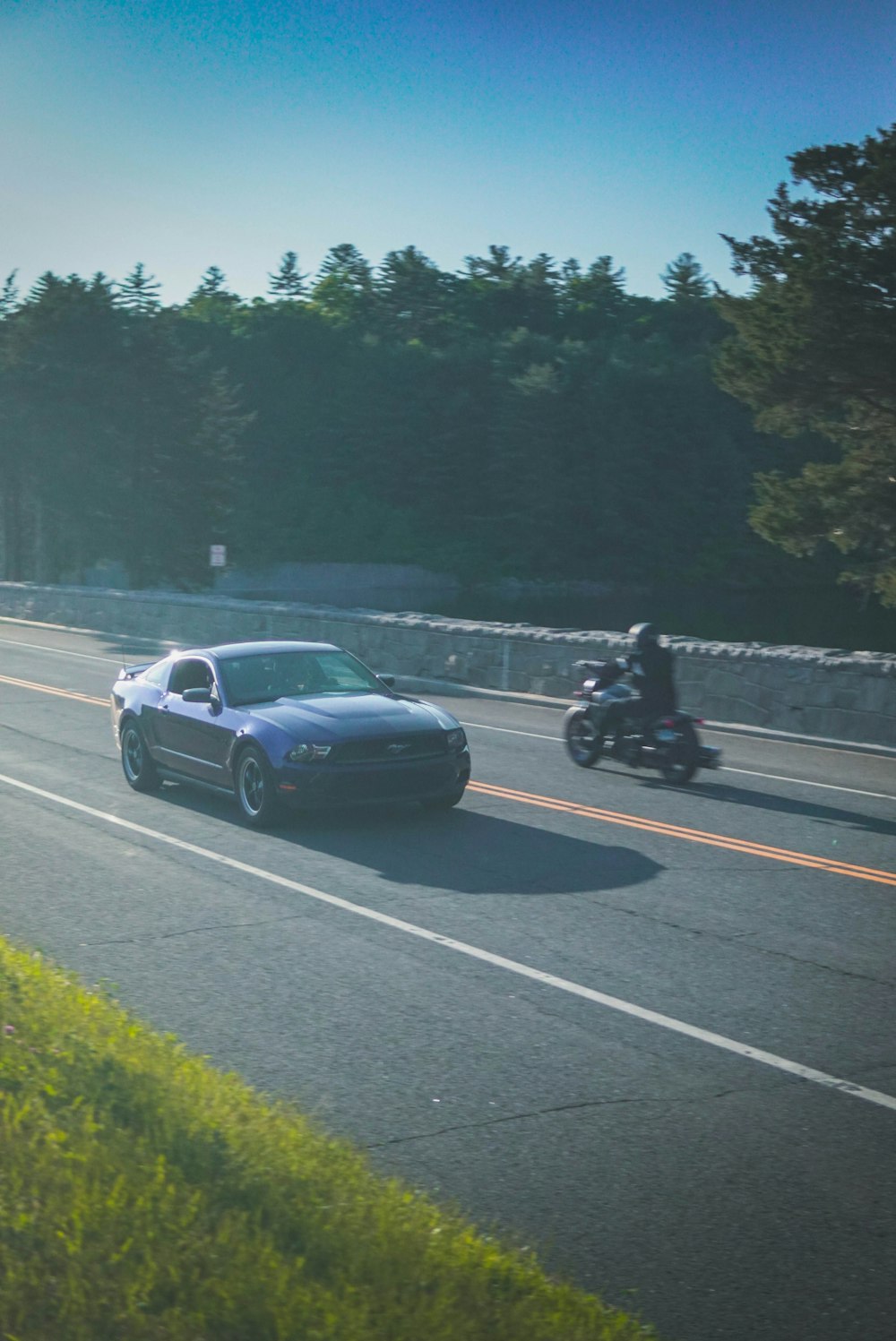 a car and a motorcycle on a road by a lake