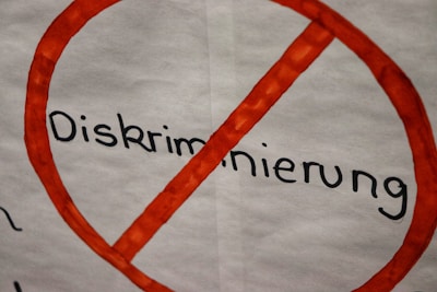 An anti-discrimination sign is depicted with the word 'Diskriminierung' crossed out in red. The background is a plain white, and the letters are bold and black.