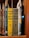 A collection of classic books on a wooden shelf, featuring titles by the author Maurice Leblanc. Prominently displayed are editions of 'Arsène Lupin Versus Herlock Sholmes' with distinctive yellow and olive covers, published by J.S. Ogilvie Publishing Company. Other featured titles include 'The Hollow Needle' and 'The Blonde Phantom.' Some book spines have decorative elements and labels are attached within the books.