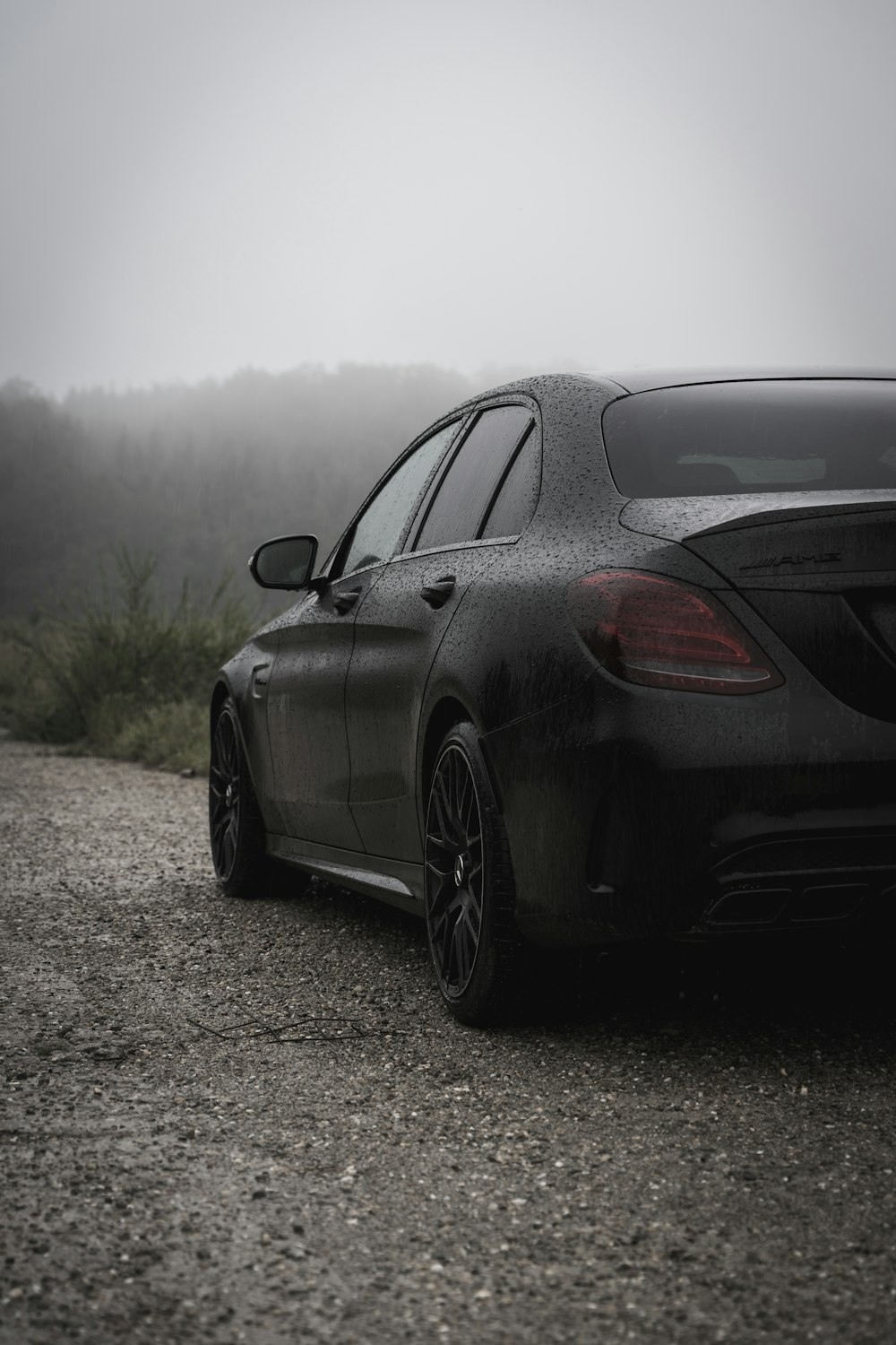 a black car parked on a dirt road with trees in the background