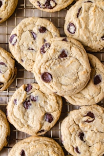 A close-up view of several freshly baked chocolate chip cookies resting on a cooling rack. The cookies are golden brown with visible dark chocolate chips embedded in the dough.
