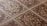 An intricate pattern of ceramic tiles with a vintage design. The tiles feature symmetrical floral motifs with a central rosette surrounded by swirling patterns. The color scheme includes earthy tones of brown, beige, and cream, emphasizing the classic and ornate style.