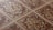 An intricate pattern of ceramic tiles with a vintage design. The tiles feature symmetrical floral motifs with a central rosette surrounded by swirling patterns. The color scheme includes earthy tones of brown, beige, and cream, emphasizing the classic and ornate style.