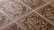 An intricate pattern of ceramic tiles with a vintage design. The tiles feature symmetrical floral motifs with a central rosette surrounded by swirling patterns. The color scheme includes earthy tones of brown, beige, and cream, emphasizing the classic and ornate style.