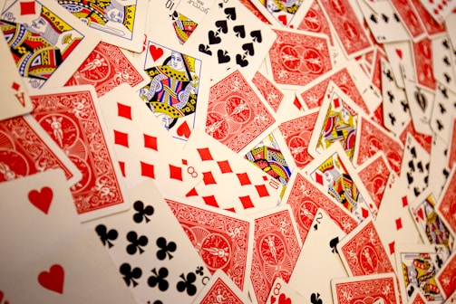 A vibrant assortment of playing cards scattered in a chaotic manner. The cards display various suits and numbers, predominantly featuring the colors red and black with intricate designs. Several face cards are visible, showcasing traditional royal characters in vivid detail.