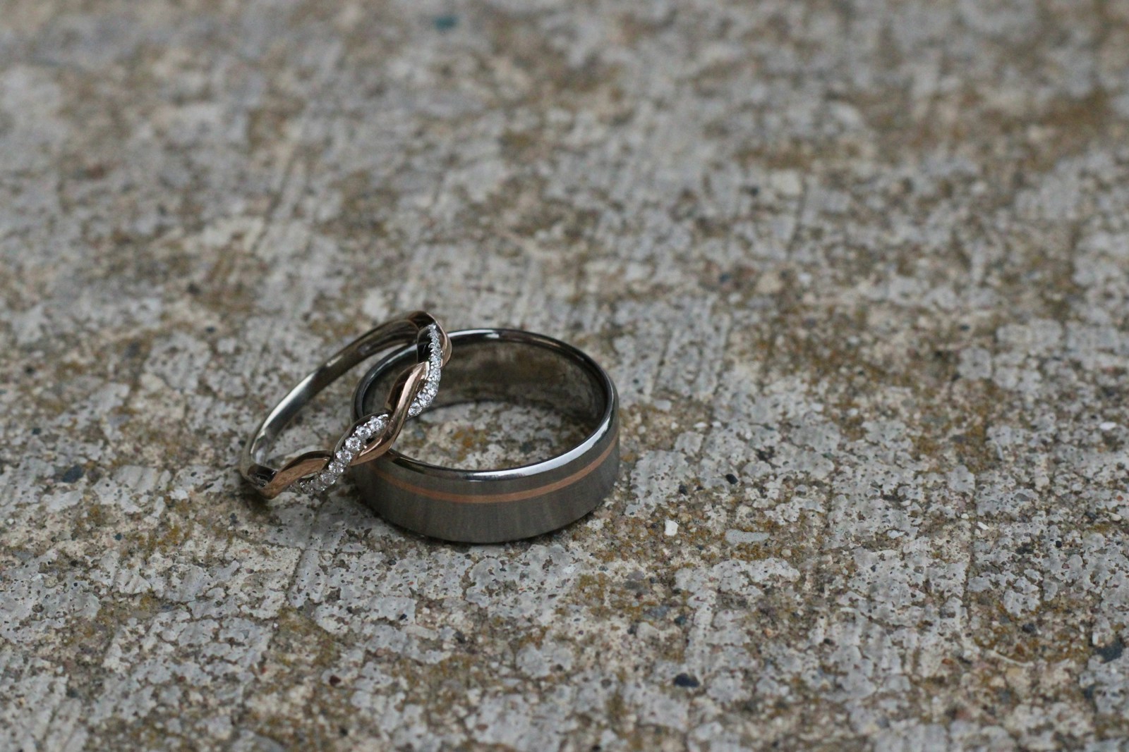Unique men's wedding band with a brushed finish and rose-gold inlay stripe resting on stone