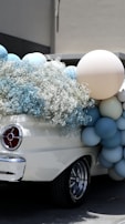 An elegant vintage car is adorned with pastel-colored balloons and delicate white flowers, creating a festive and charming atmosphere.