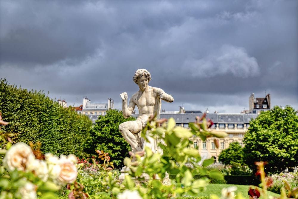 a statue of a person in a garden with buildings in the background