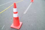 Close-up of a bright orange traffic cone with reflective stripes on a busy road site.