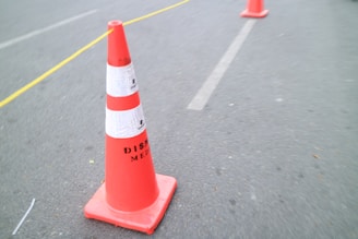 A bright orange traffic cone placed on a paved street.
