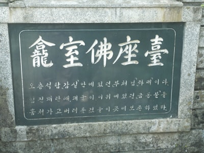 A stone plaque featuring Korean text inscribed on a dark background, bordered by a light gray stone frame. The text is large and prominent at the top, with smaller characters below.