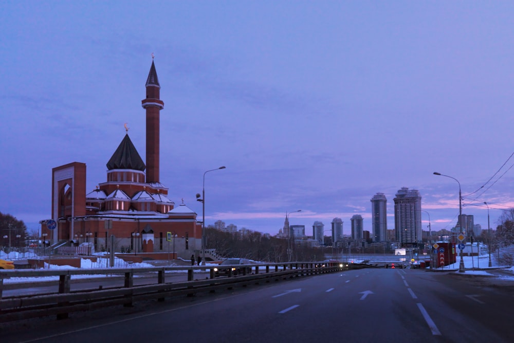 a road with a building on the side and a city in the background