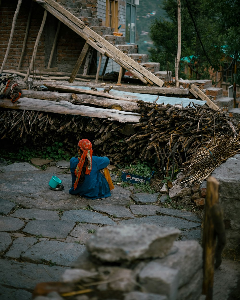 a person sitting on a stone path next to a pile of wood